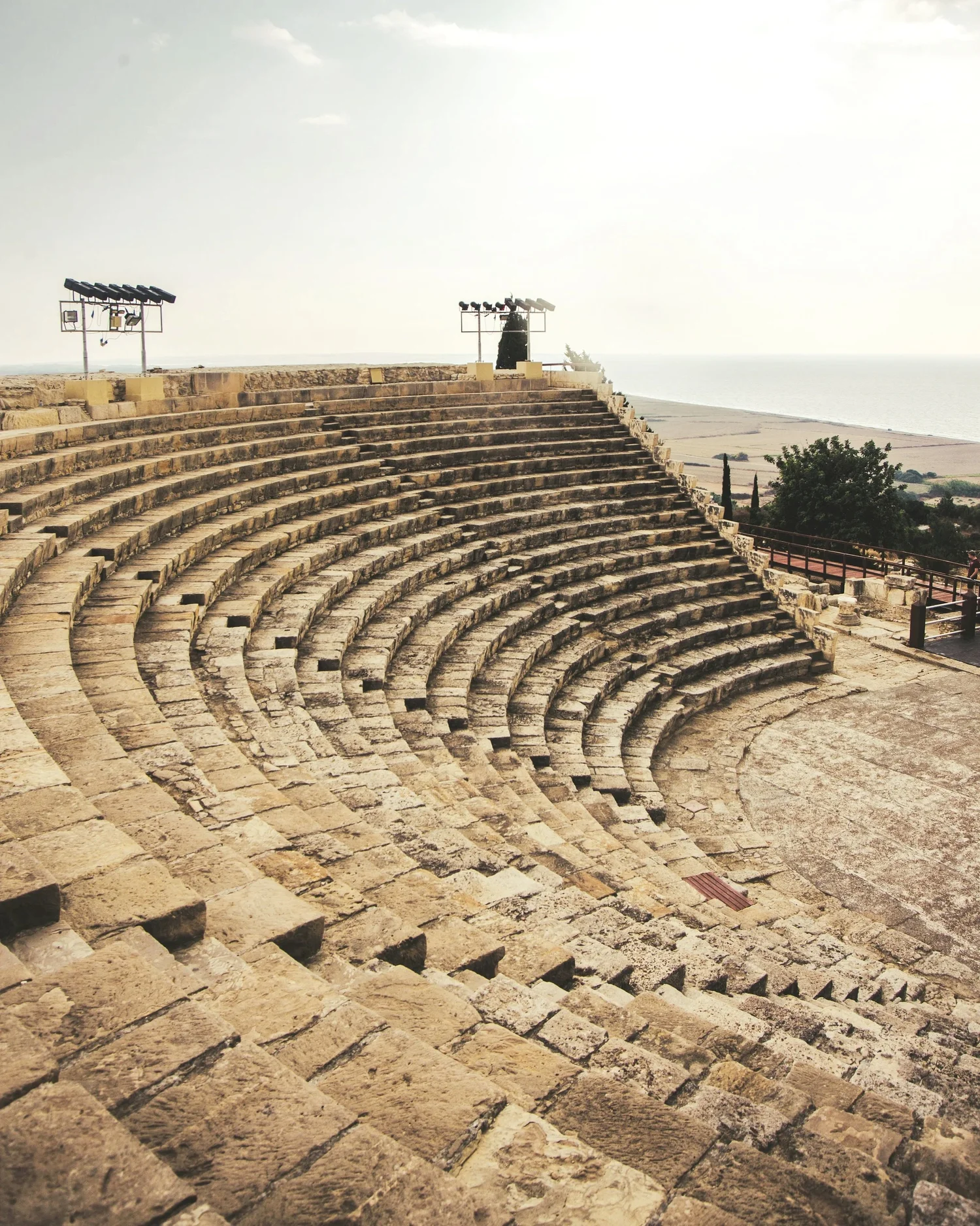 Ancient stone amphitheater with curved seating facing the sea, with stage area in front.