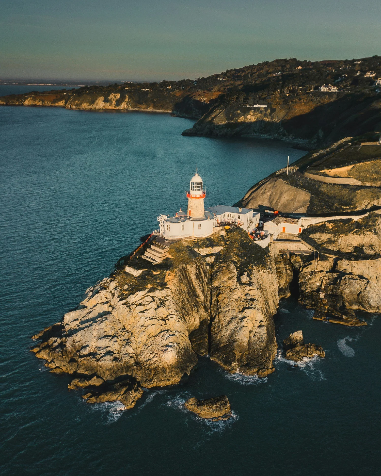 A lighthouse on a rocky island surrounded by water, with a coastal landscape in the background.