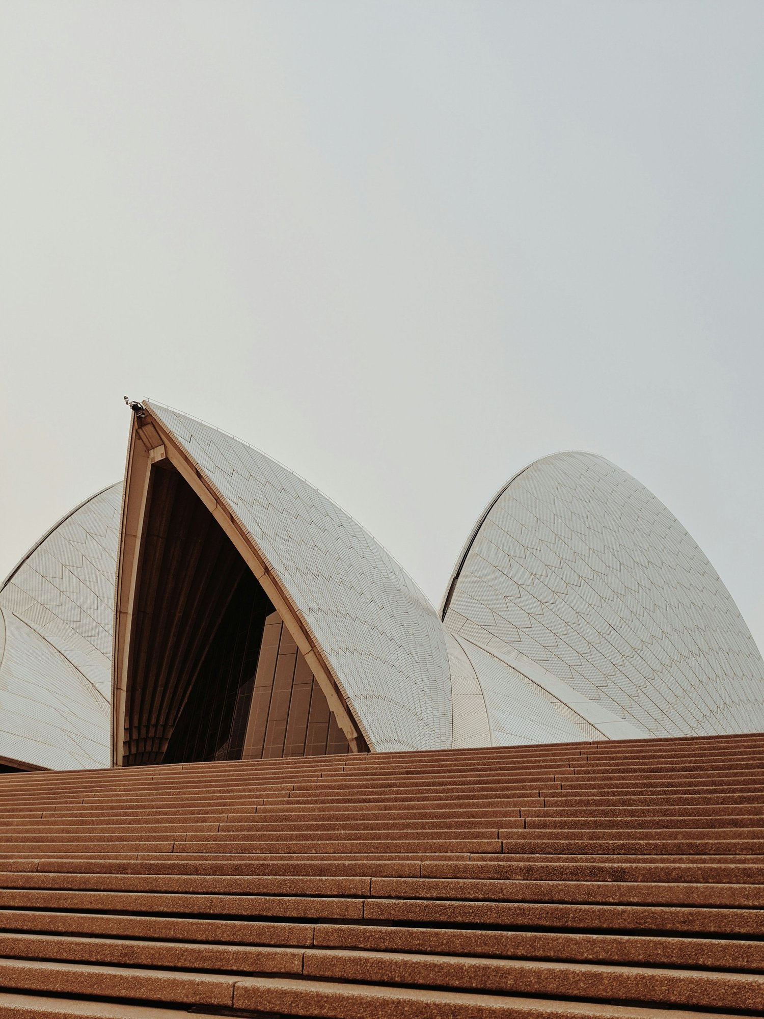 Close-up view of the Sydney Opera House with stairs in the foreground and cloudy sky in the background.