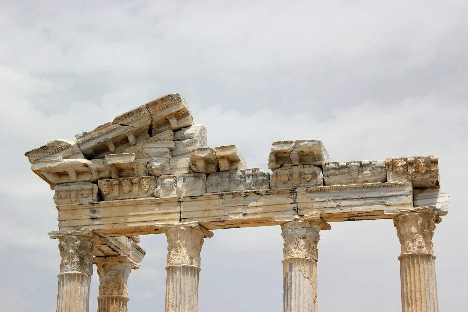 Ancient Greek ruins with partially intact columns and stone architecture against cloudy sky.