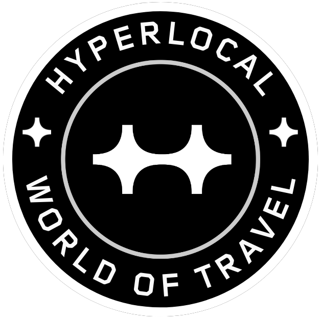 Black and white circular badge with the words ‘HYPERLOCAL WORLD OF TRAVEL’ around the edges and a stylized airplane symbol in the center.