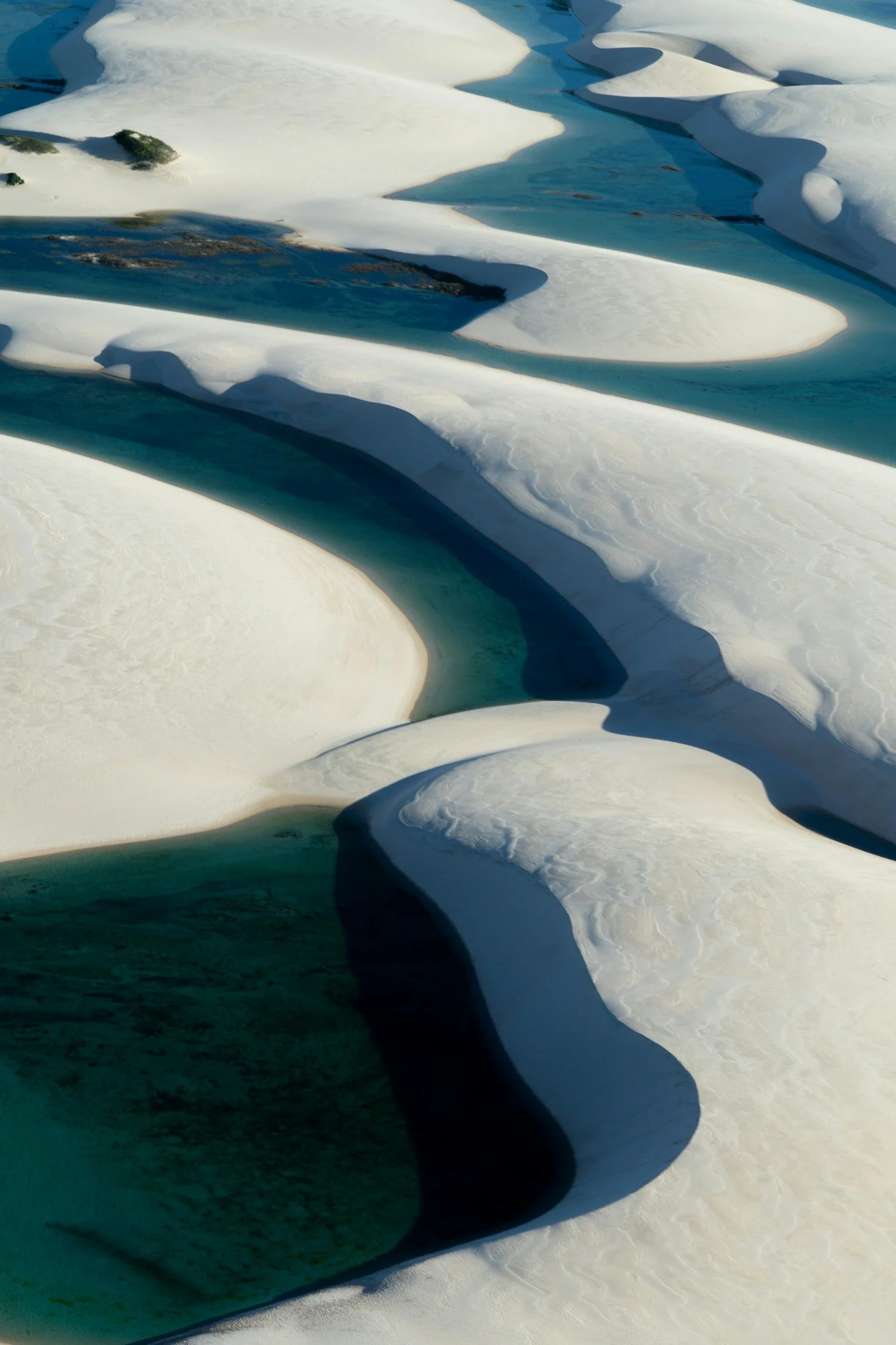 Aerial view of snow and ice formations with turquoise water channels in a polar landscape.