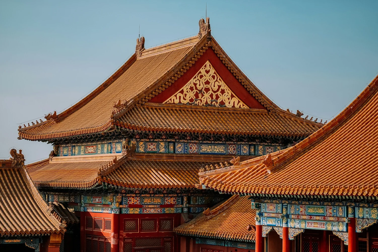 Traditional Chinese palace roof with ornate carvings, colorful painted designs, and tiled rooftops under a clear sky.