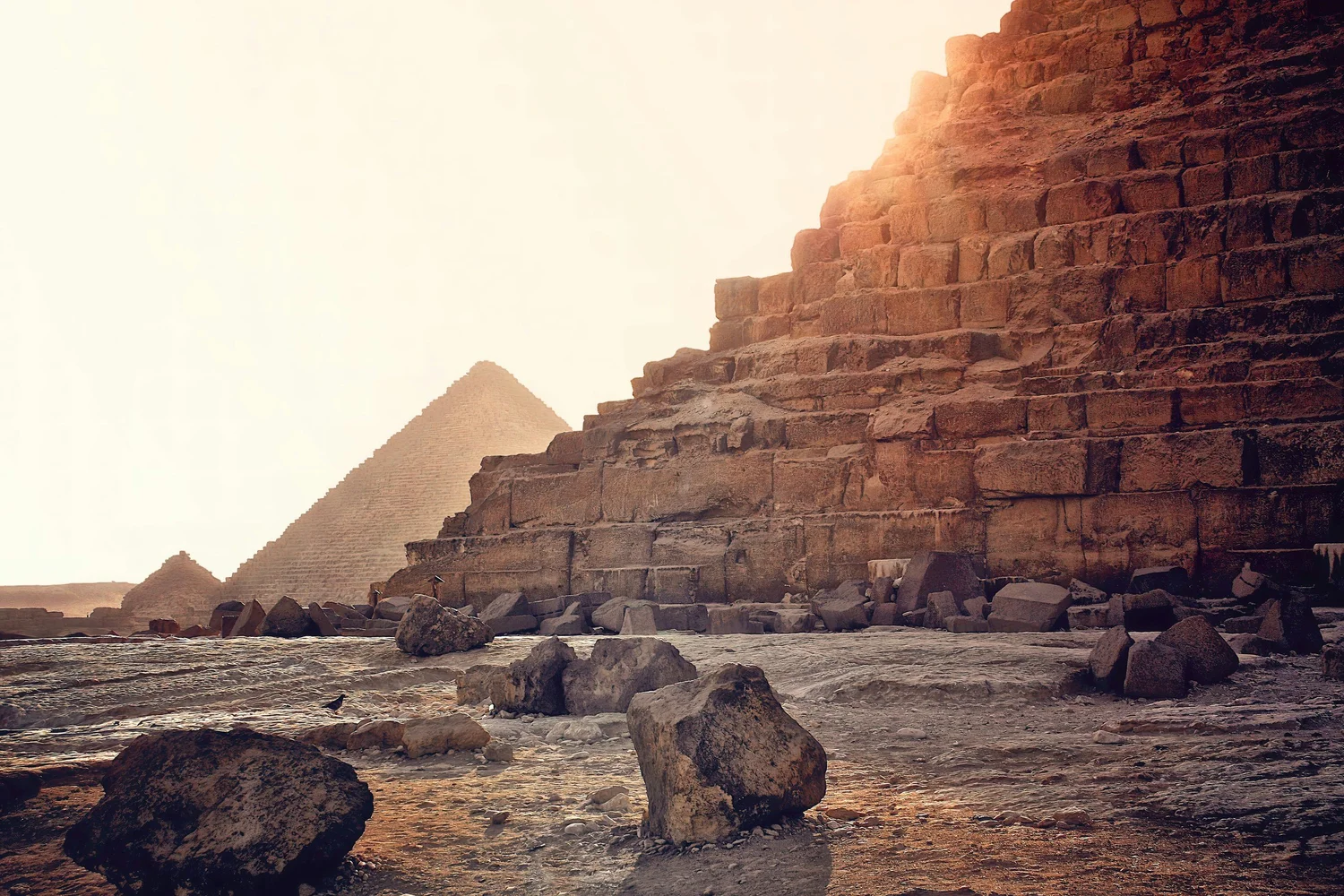 Ancient pyramids in Egypt with rocks in the foreground and sunlight in the background.