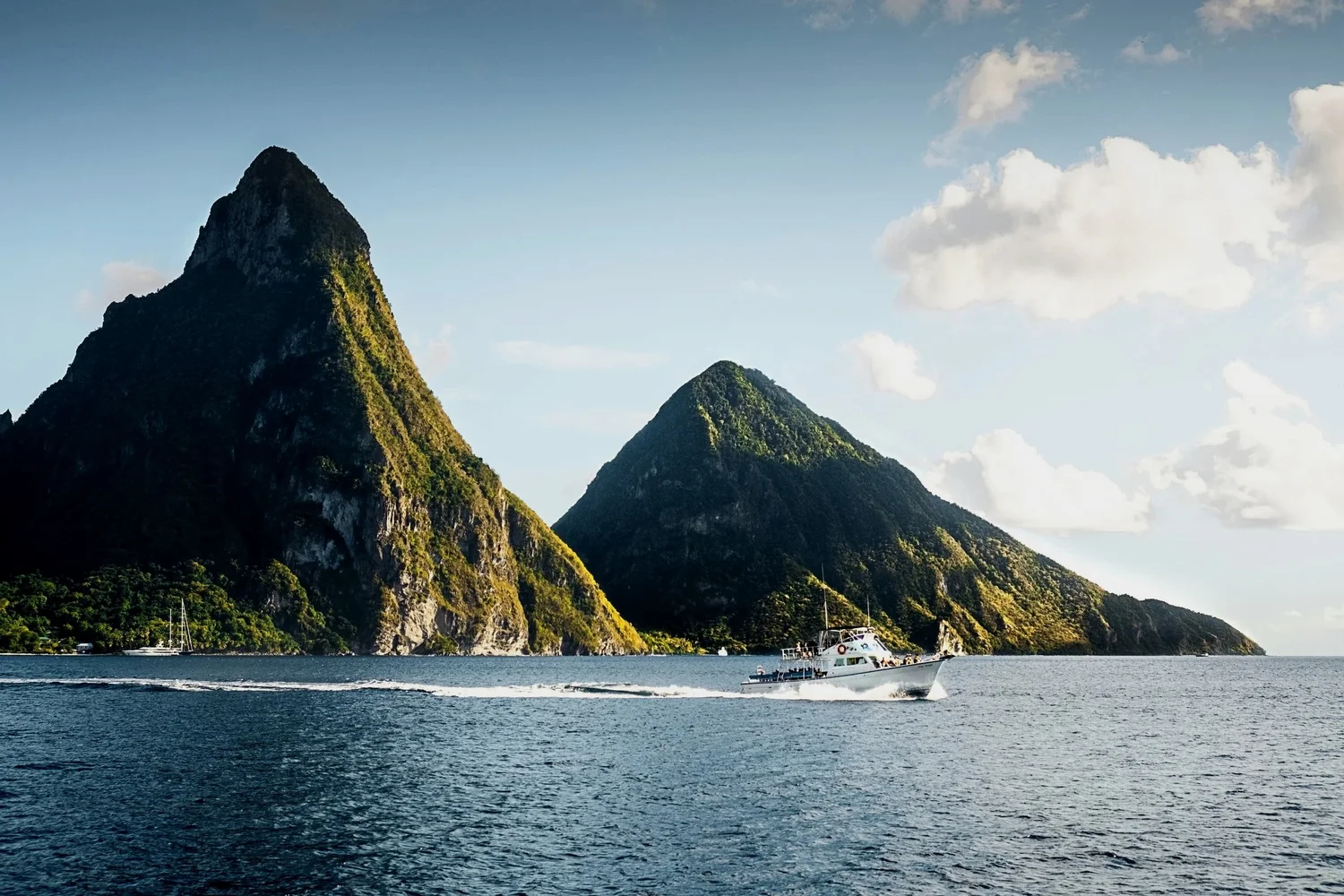 A boat sailing near green, mountainous islands with partly cloudy sky.
