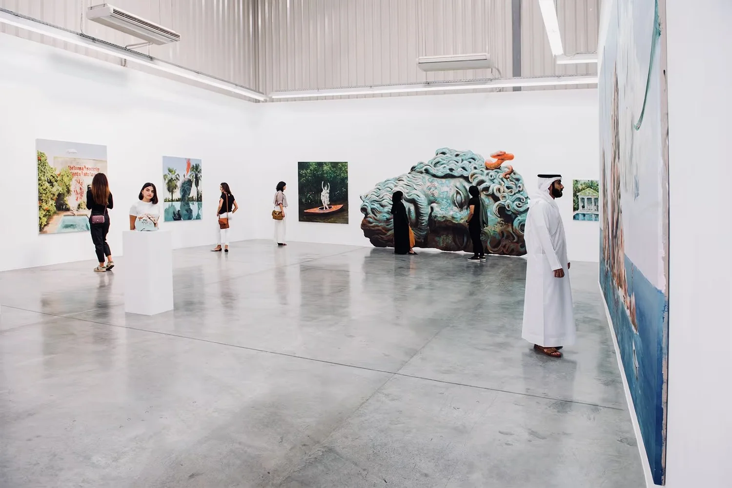 People viewing various artworks in a modern art gallery with white walls and concrete floors.