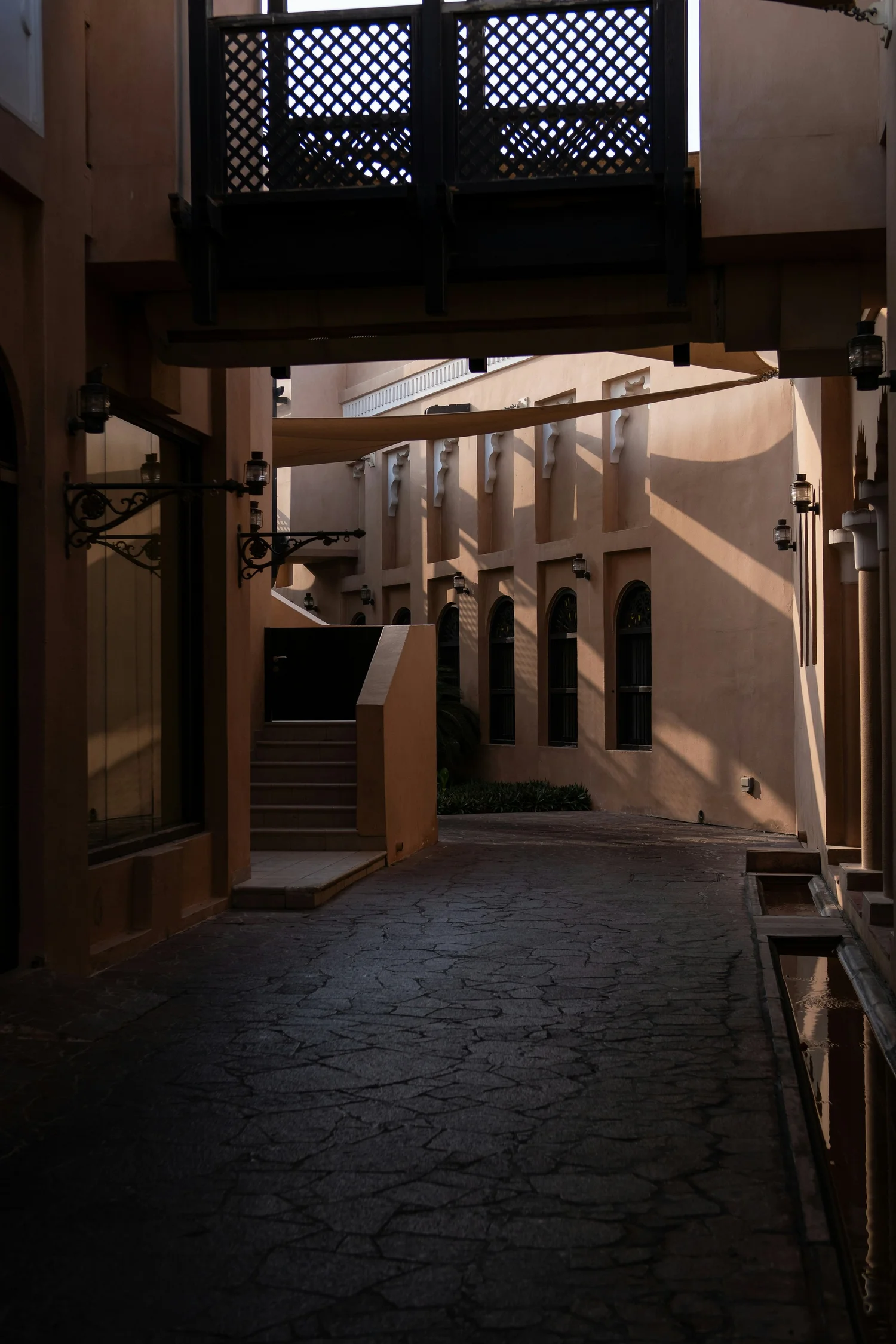 An alleyway with peach-colored walls, arched windows, stone pavement, and decorative wrought iron lanterns.