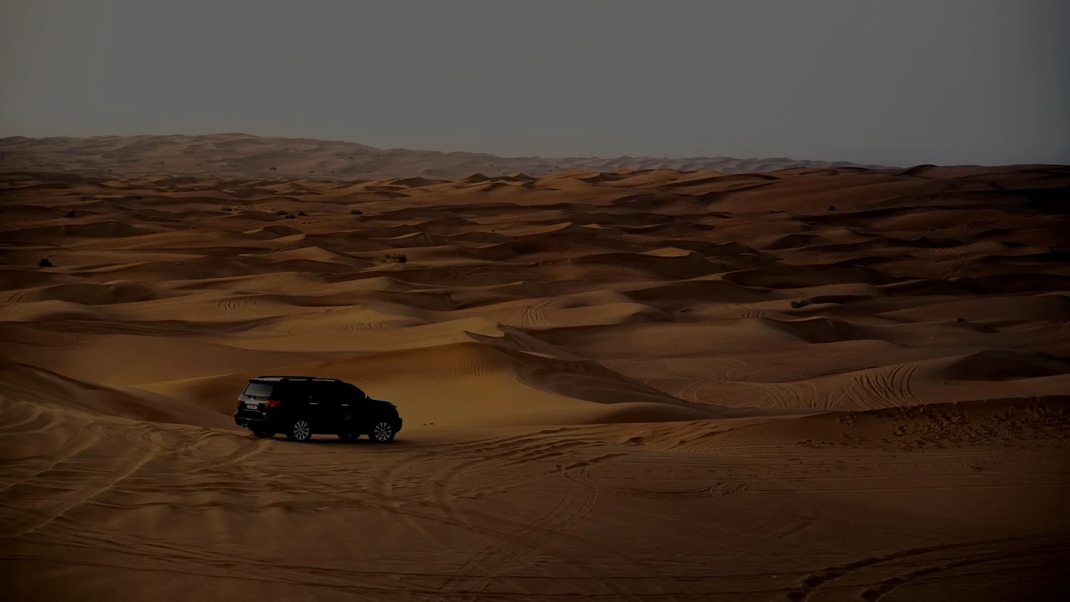 A black SUV parked on sand dunes in a desert landscape with a clear sky.