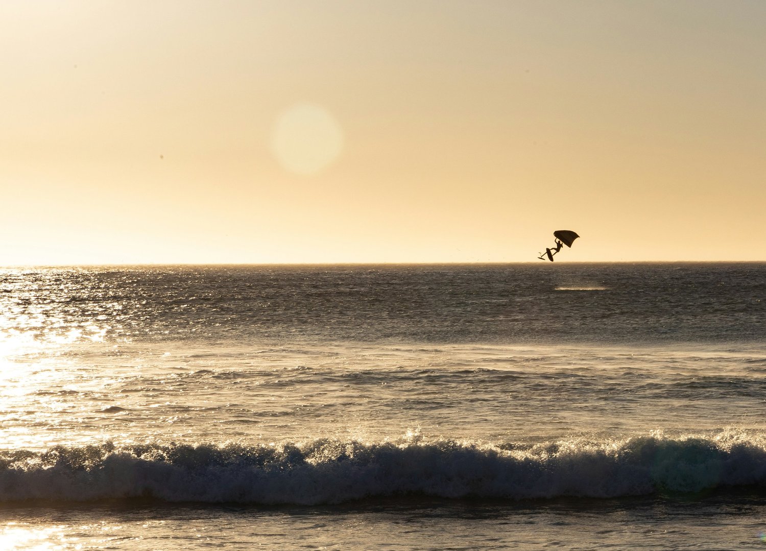 A person performing a jump with a parachute over the ocean during sunset.