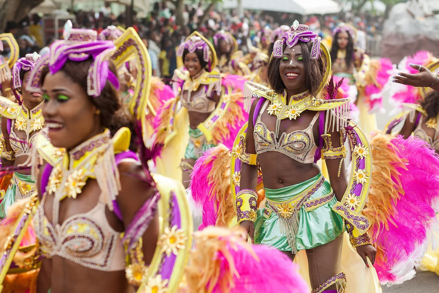 Women dressed in colorful costumes with feathers, beads, and jewelry, participating in a parade or festival, smiling and enjoying the event.