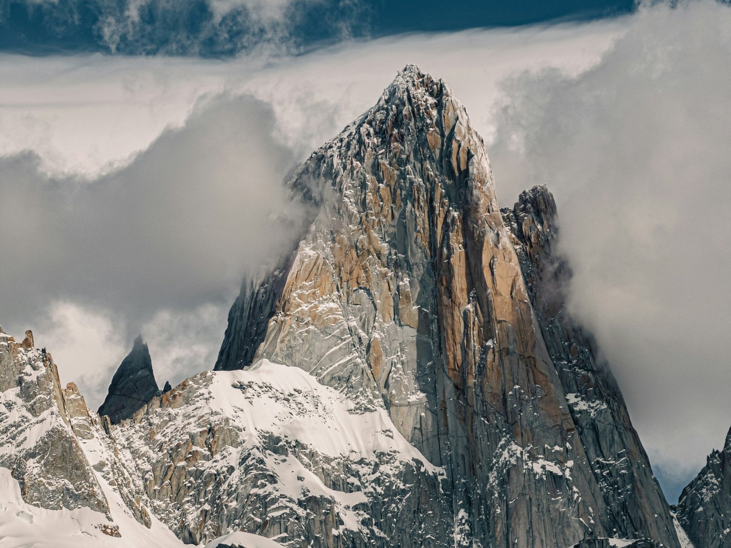 Snow-covered rugged mountain peak surrounded by clouds.