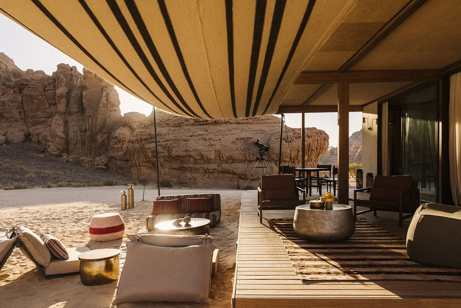 Outdoor lounge area with modern furniture, a telescope, and desert rock formations in the background.