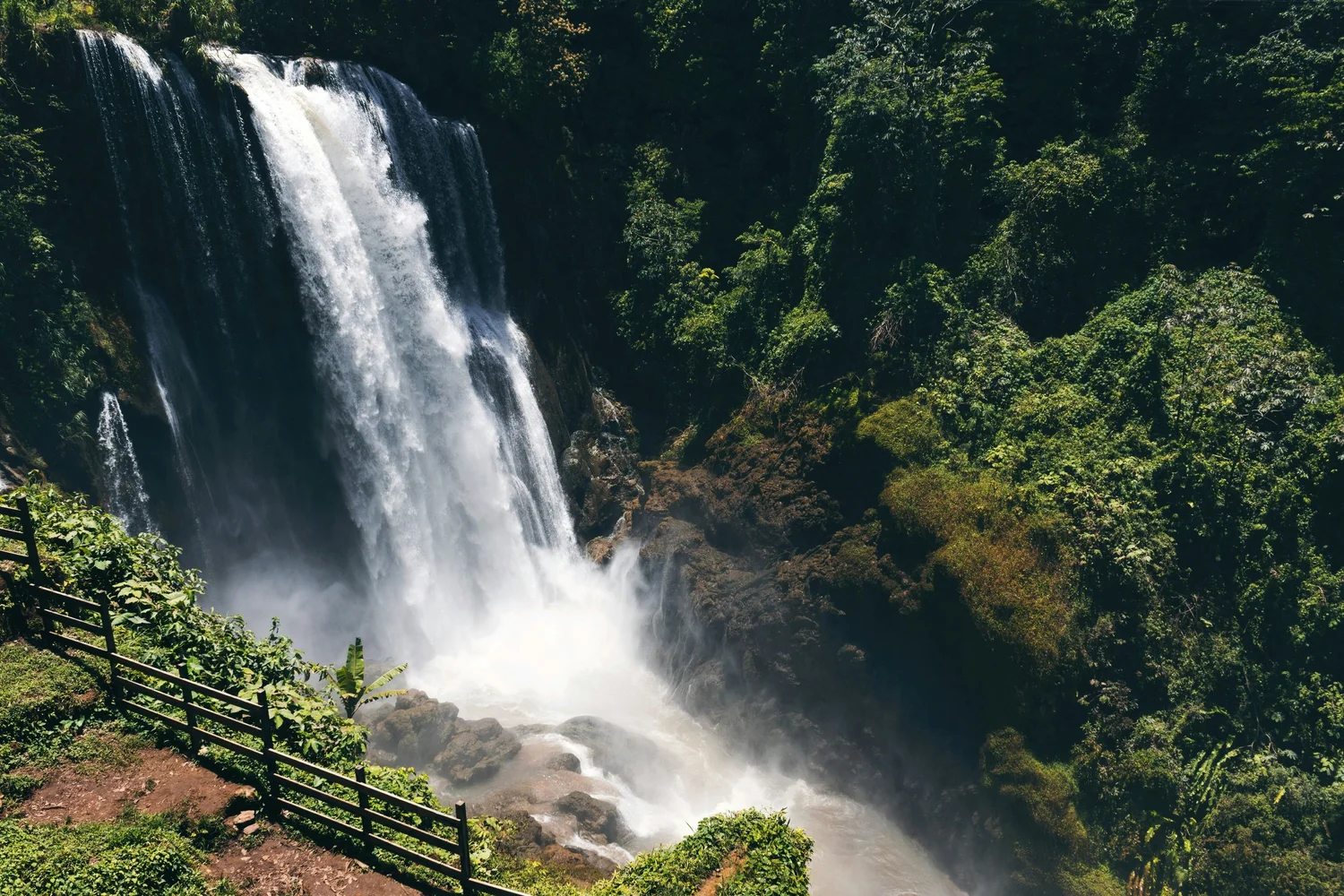 A large waterfall flowing down into a rocky stream surrounded by lush green trees and vegetation.