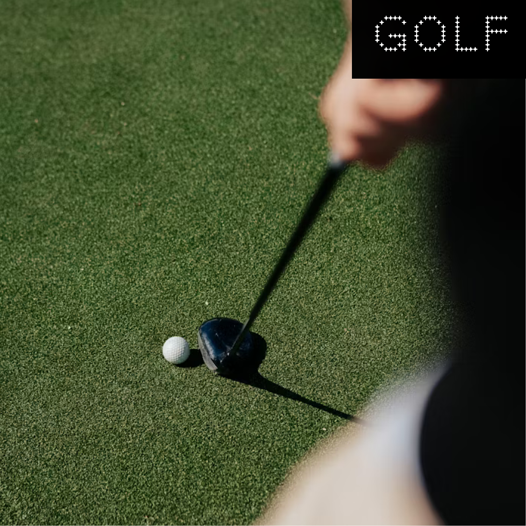 Close-up of a person preparing to putt a golf ball on the putting green with a golf club, with the word 'GOLF' in dotted letters in the top right corner.