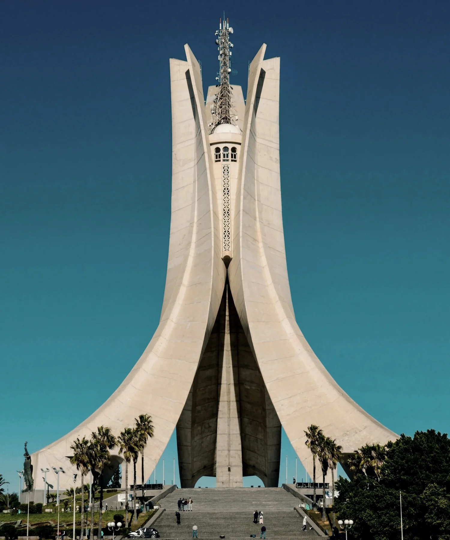 A tall, modern monument with curved, white concrete structures and an antenna on top, set against a clear blue sky.