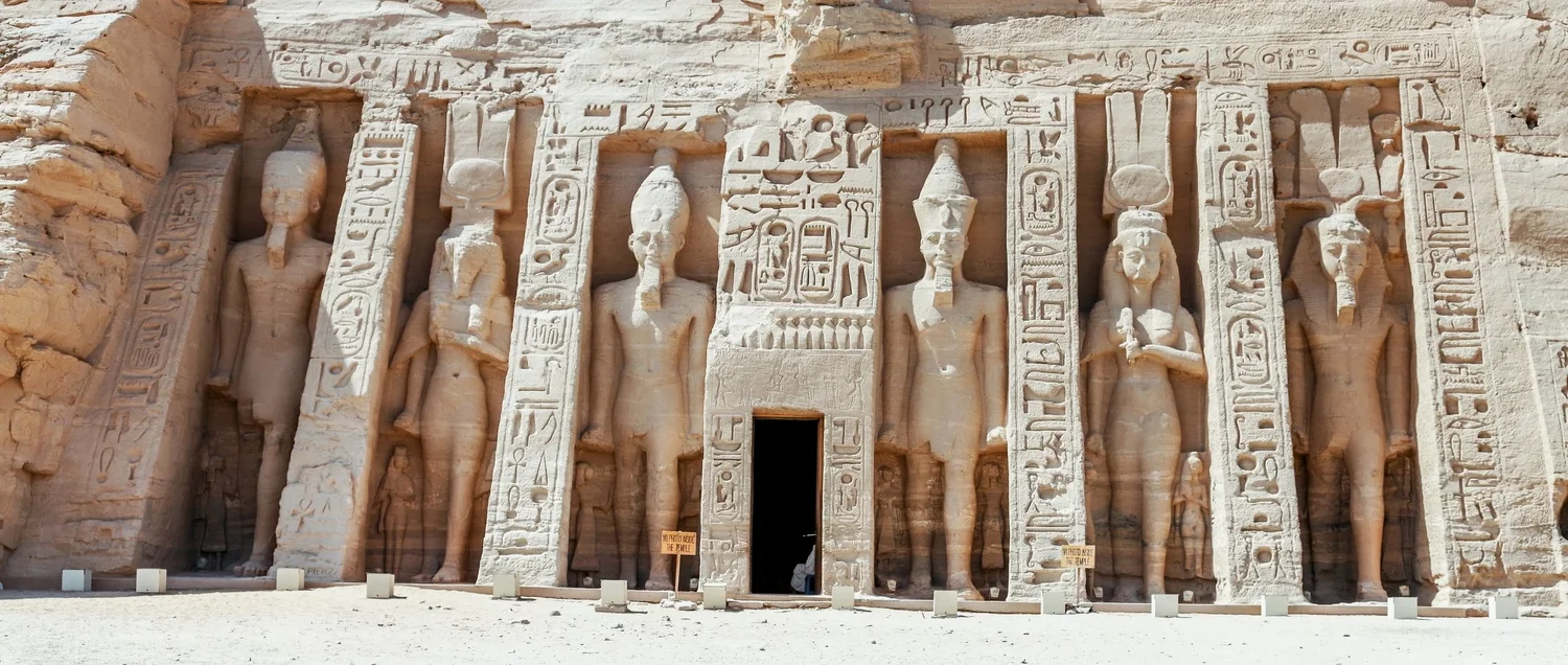 Ancient Egyptian temple entrance with large statues and hieroglyphics carved into stone walls.