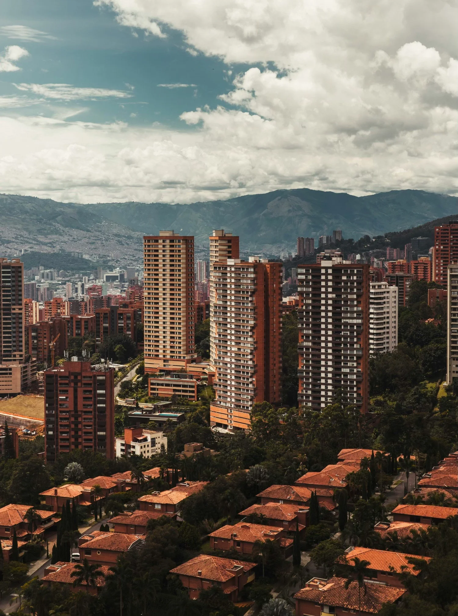 Cityscape with high-rise buildings and mountains in the background under a partly cloudy sky.