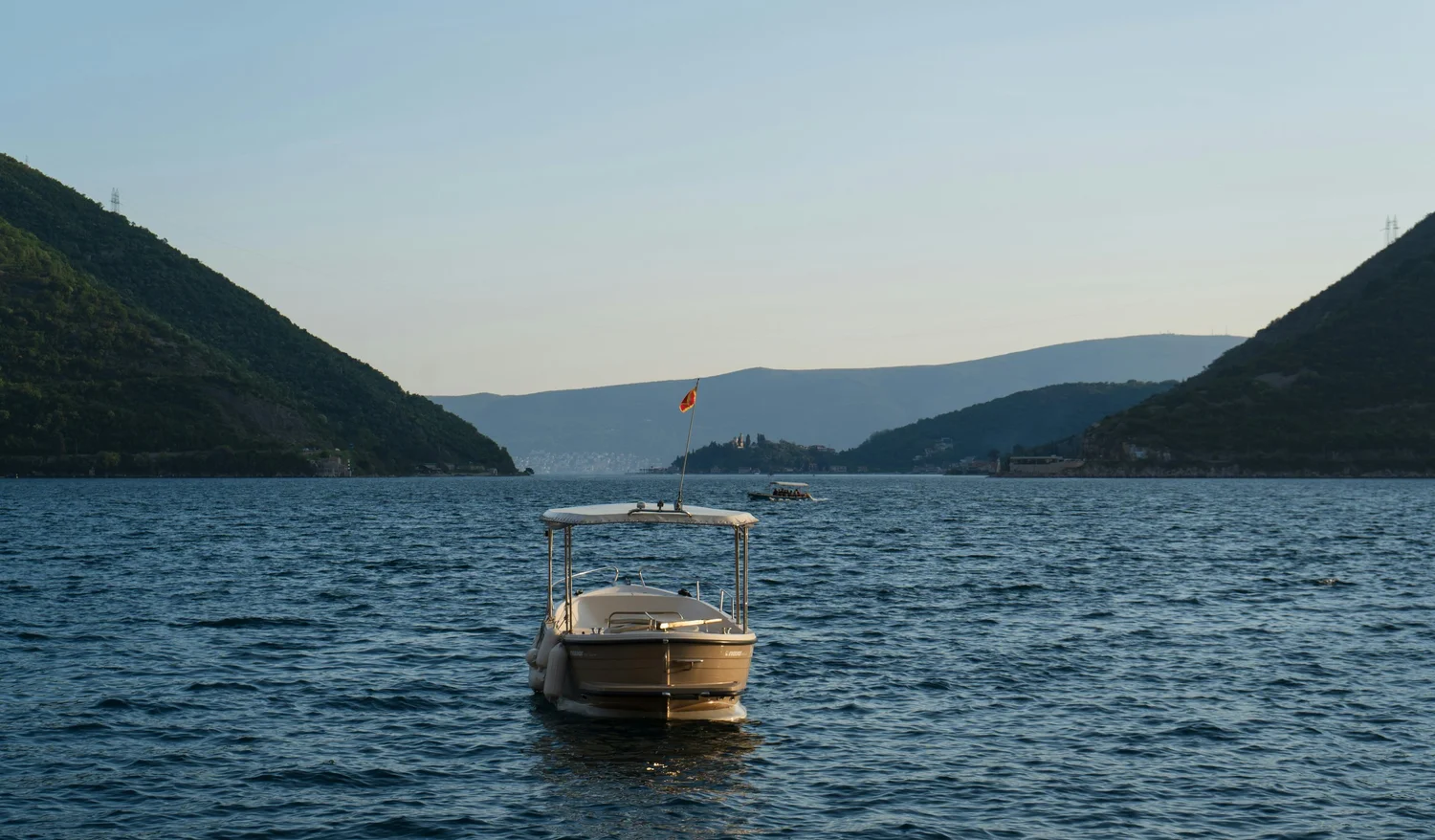 A boat floating on a lake surrounded by green hillside mountains with a small boat in distance