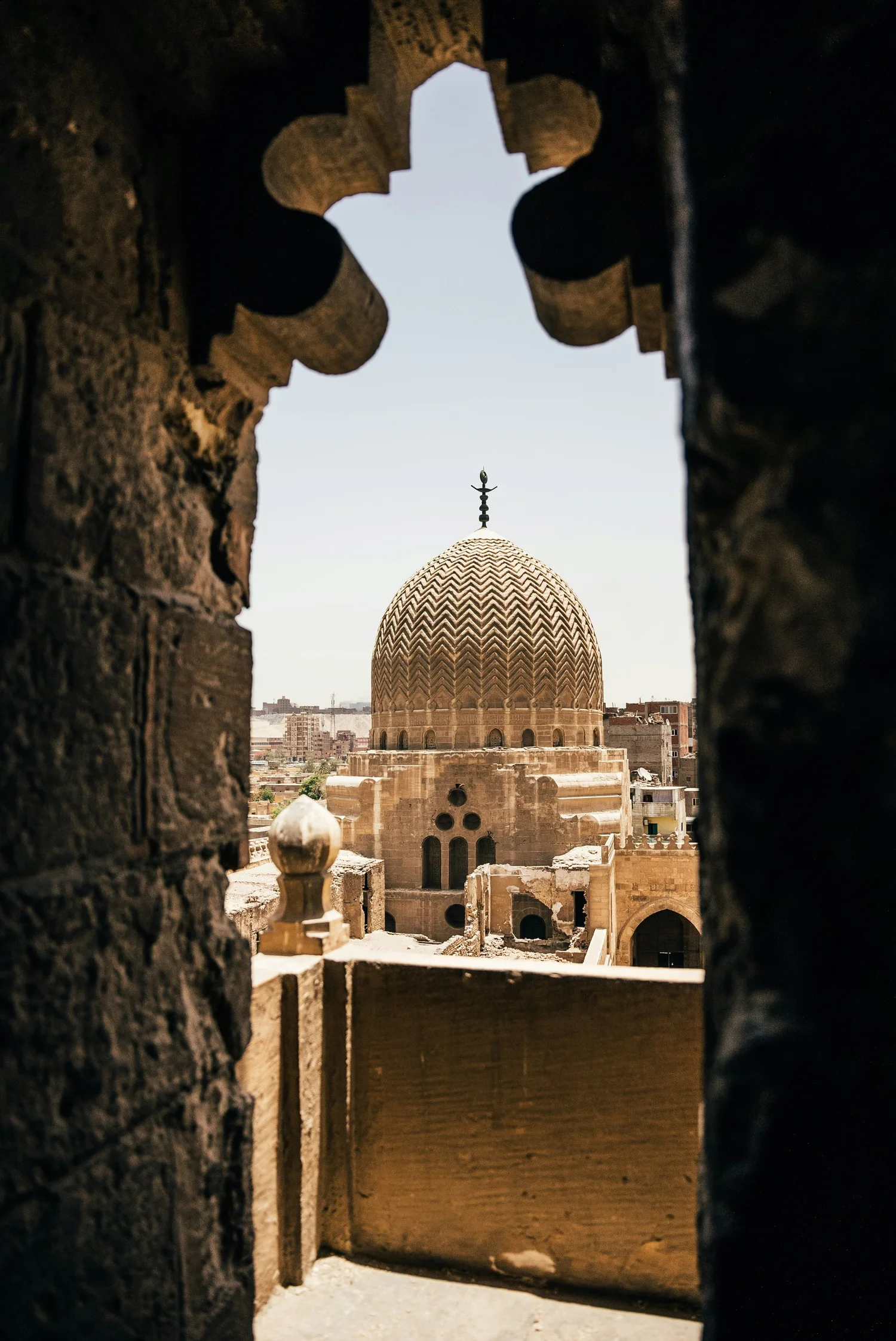View of a building with a patterned dome through a decorative stone window.