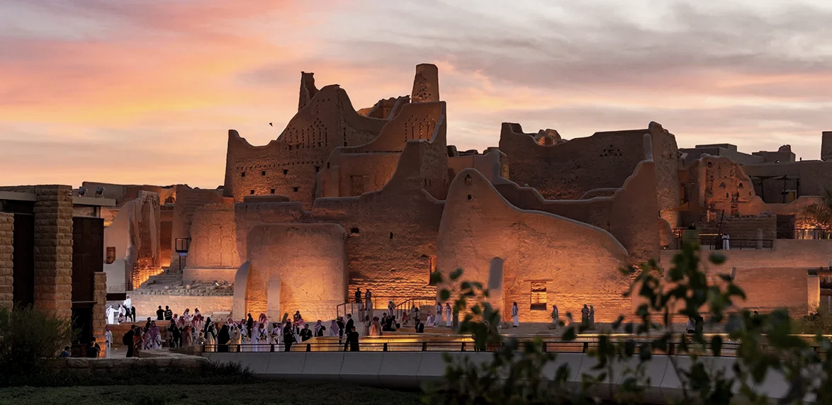 Ancient clay fortresses illuminated during sunset with people walking in the foreground.