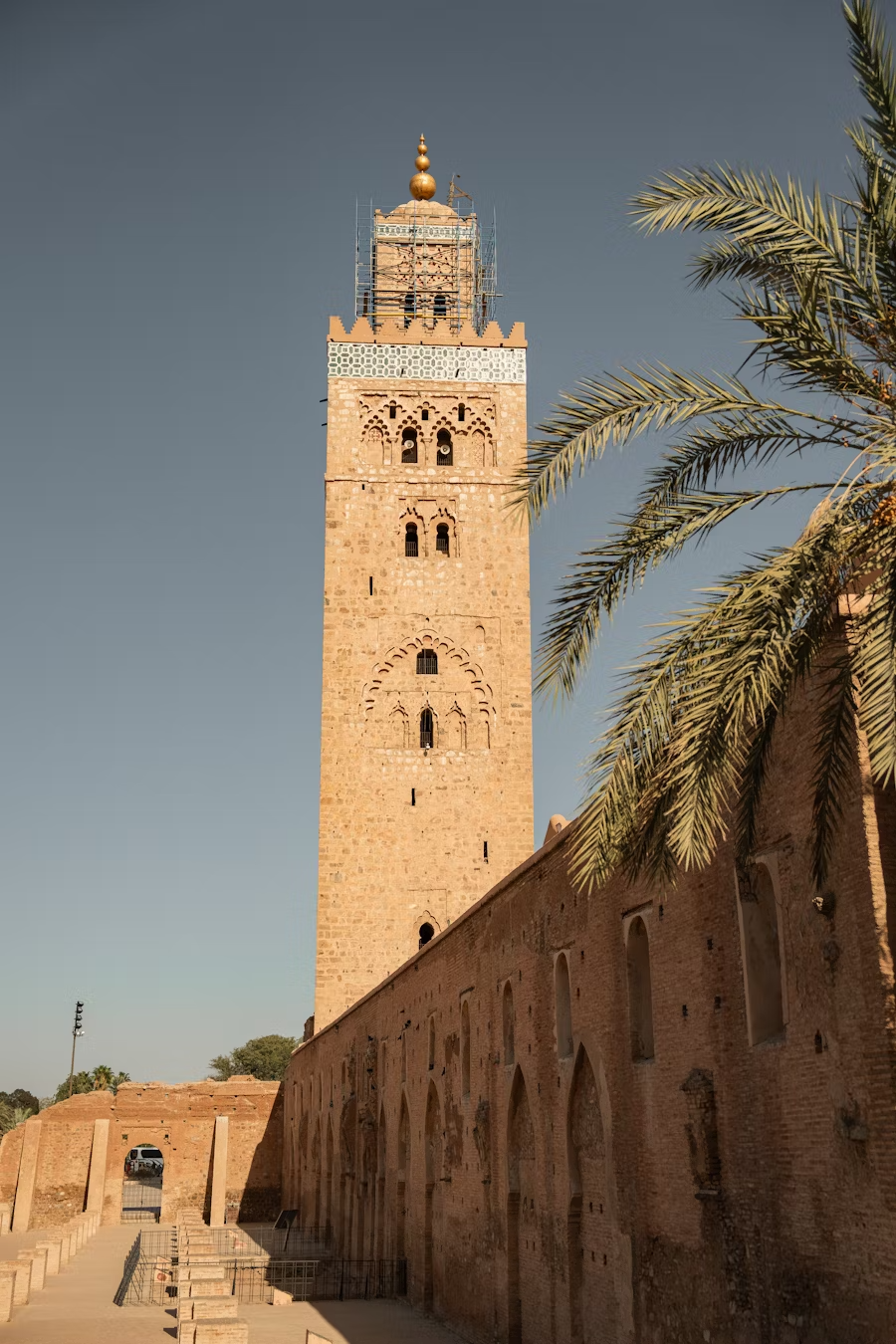Tall historic minaret with Islamic architectural details, surrounded by palm trees against a clear sky.