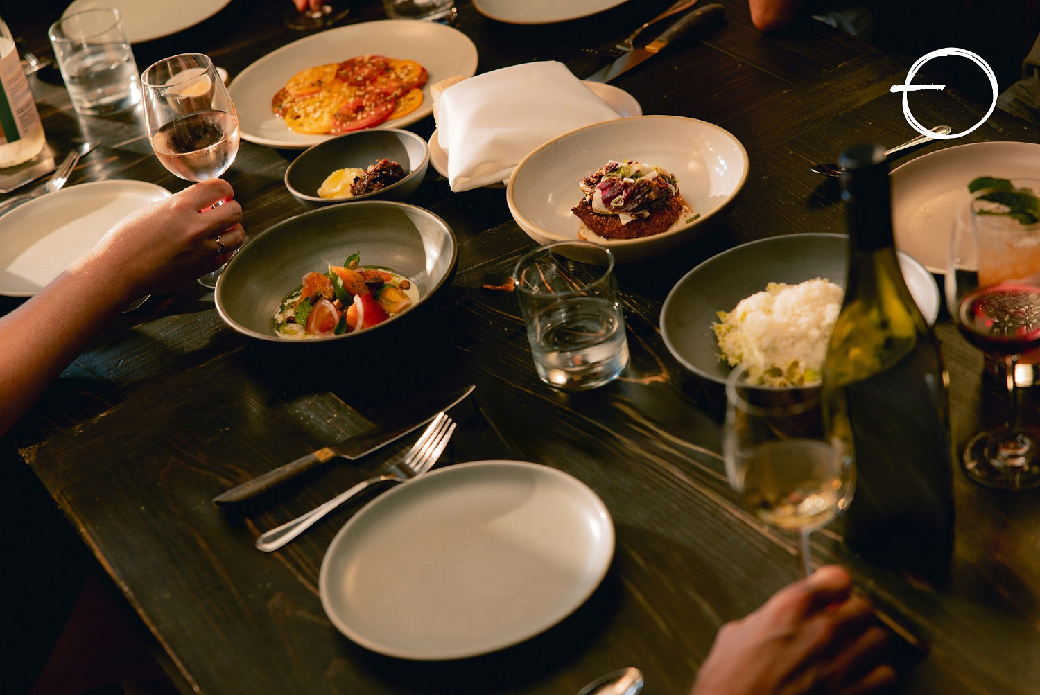 A dinner table set with various plates of food, glasses of water and wine, and utensils, with some dishes partially eaten.
