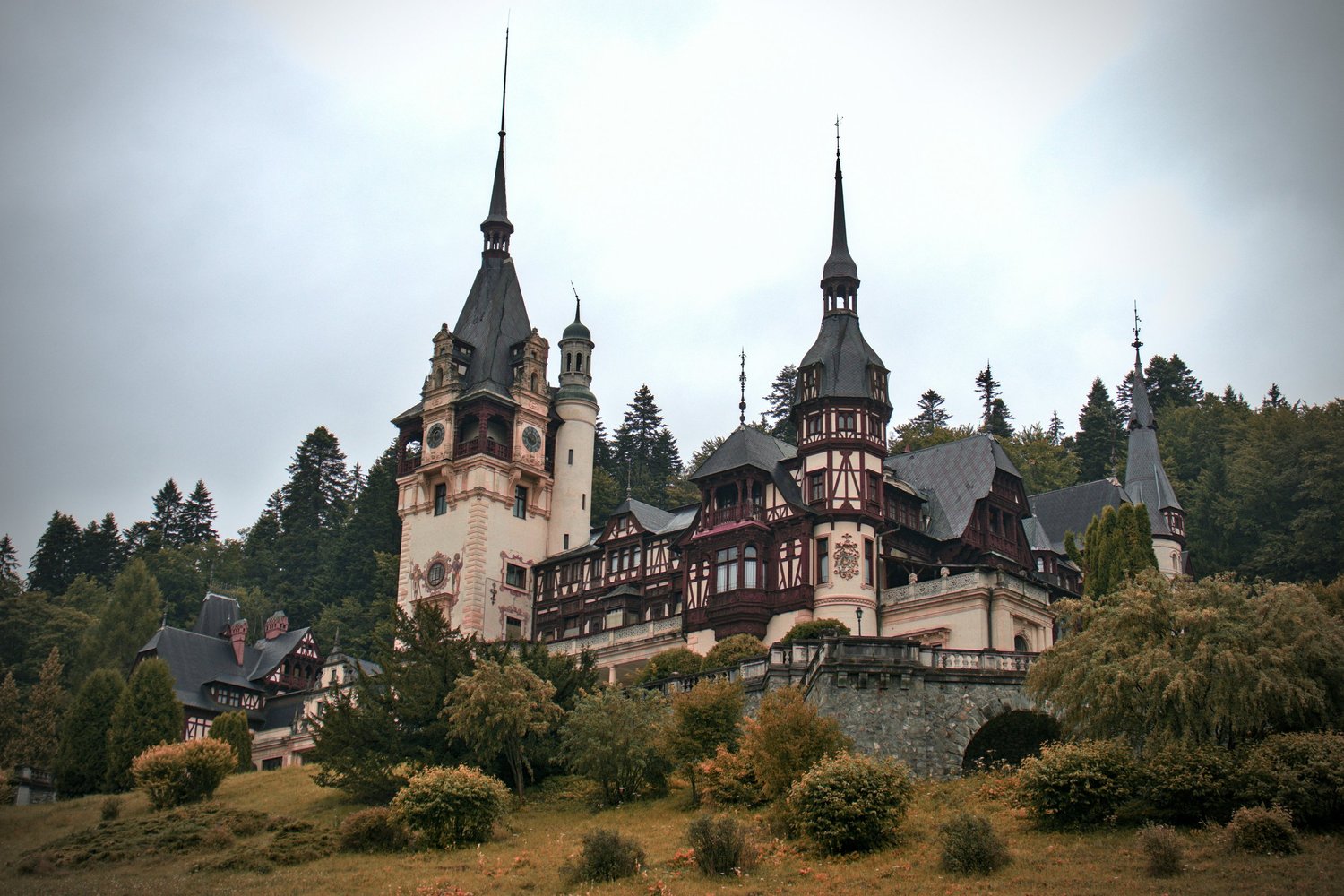 A fairy tale castle with multiple towers and spires, set on a hill surrounded by trees and greenery.
