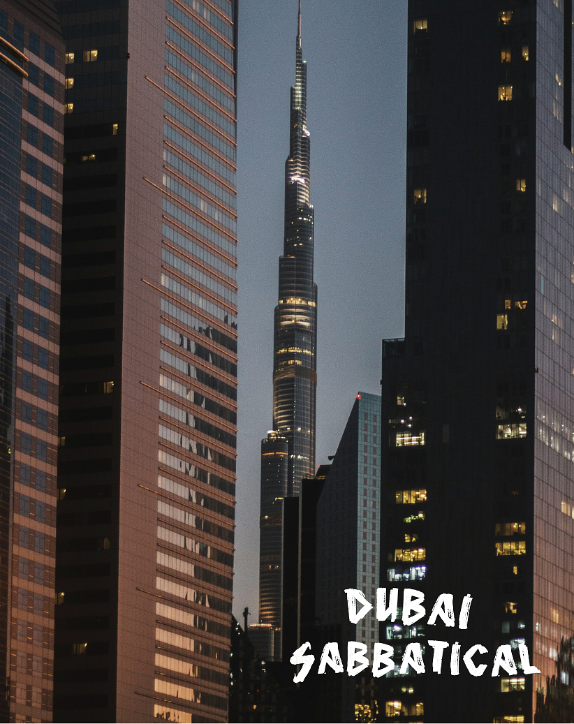 Nighttime cityscape featuring the Burj Khalifa towering between high-rise office buildings in Dubai, with city lights visible. Text overlay reads 'Dubai Sabbatical'.