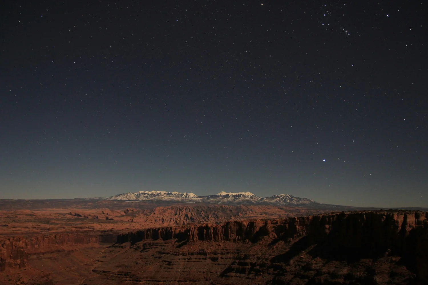 Nighttime view of desert landscape with snow-capped mountains under a starry sky. Hyperlocal World of Travel.