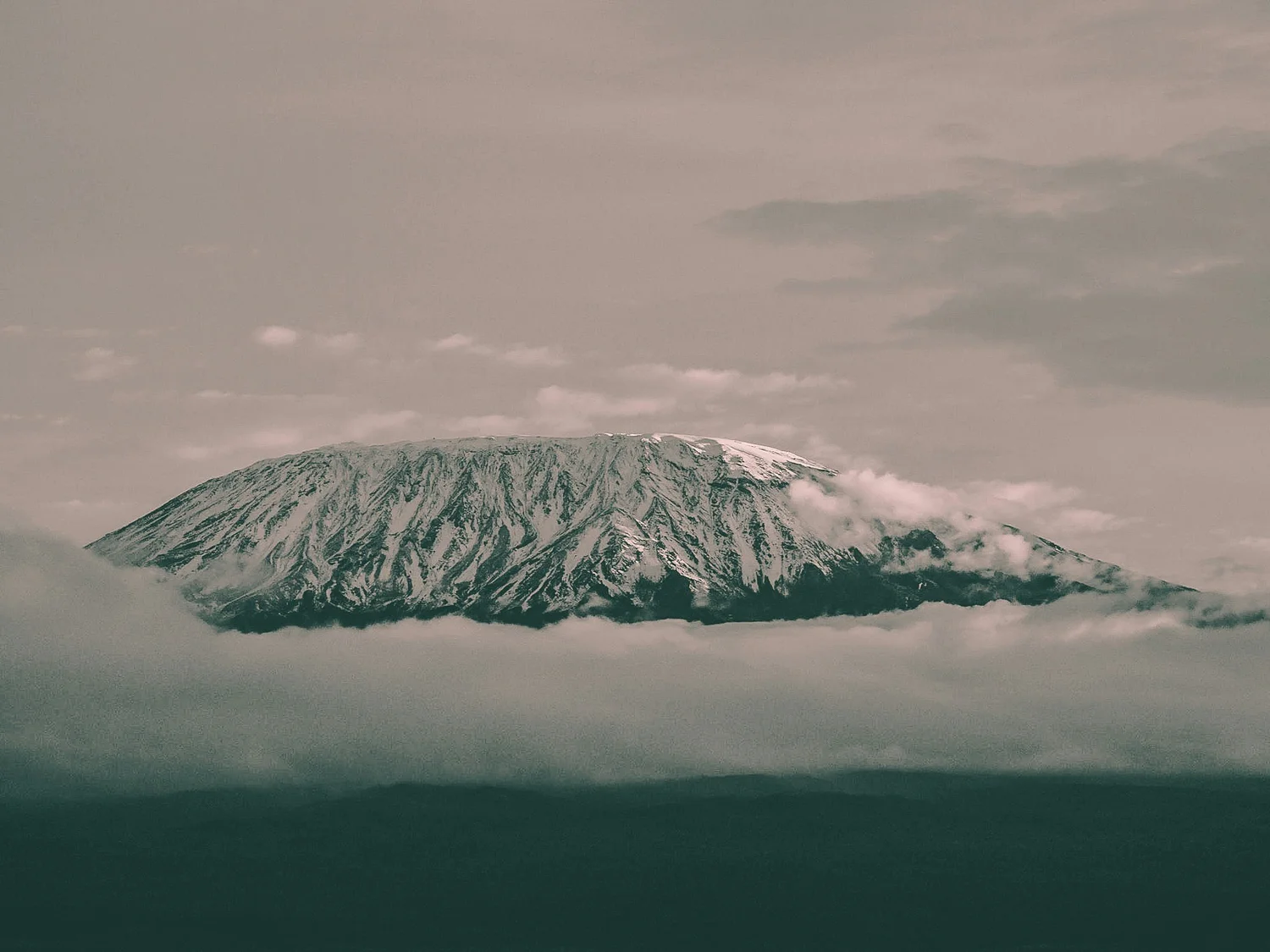 A snow-capped mountain, possibly a volcano, surrounded by clouds and mist.