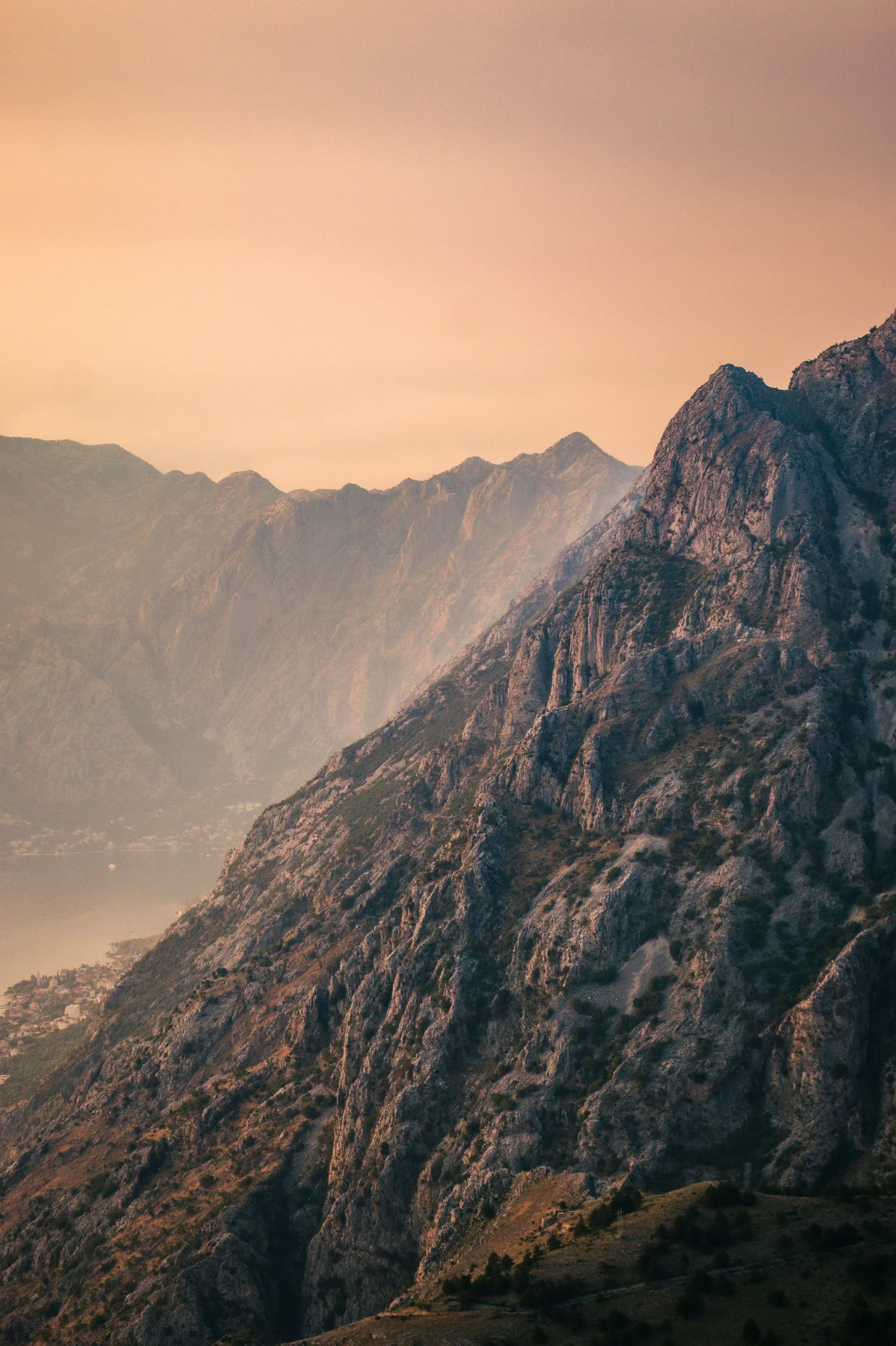 Mountain landscape with large rocky peaks, some greenery, and a hazy sky at dusk or dawn.