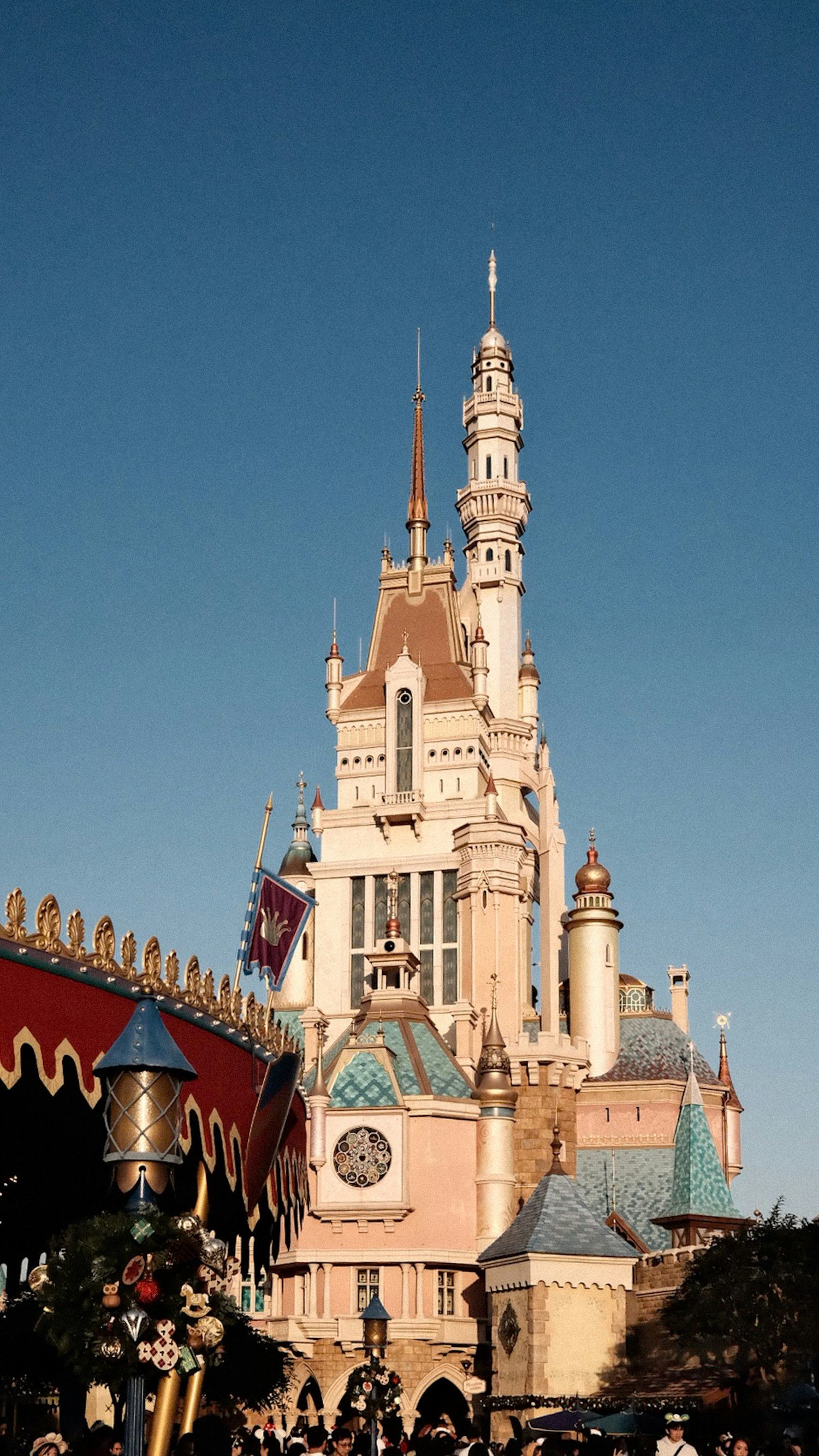 Disney Castle at Disneyland with blue sky, decorated with holiday ornaments and crowd of visitors in foreground.