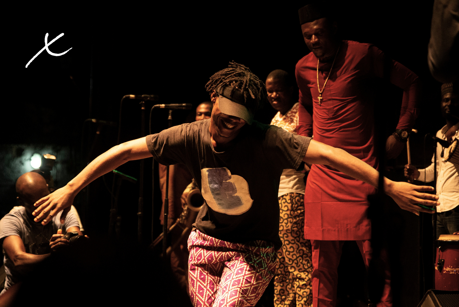 A person dancing joyfully on stage, surrounded by musicians and onlookers at a lively event.