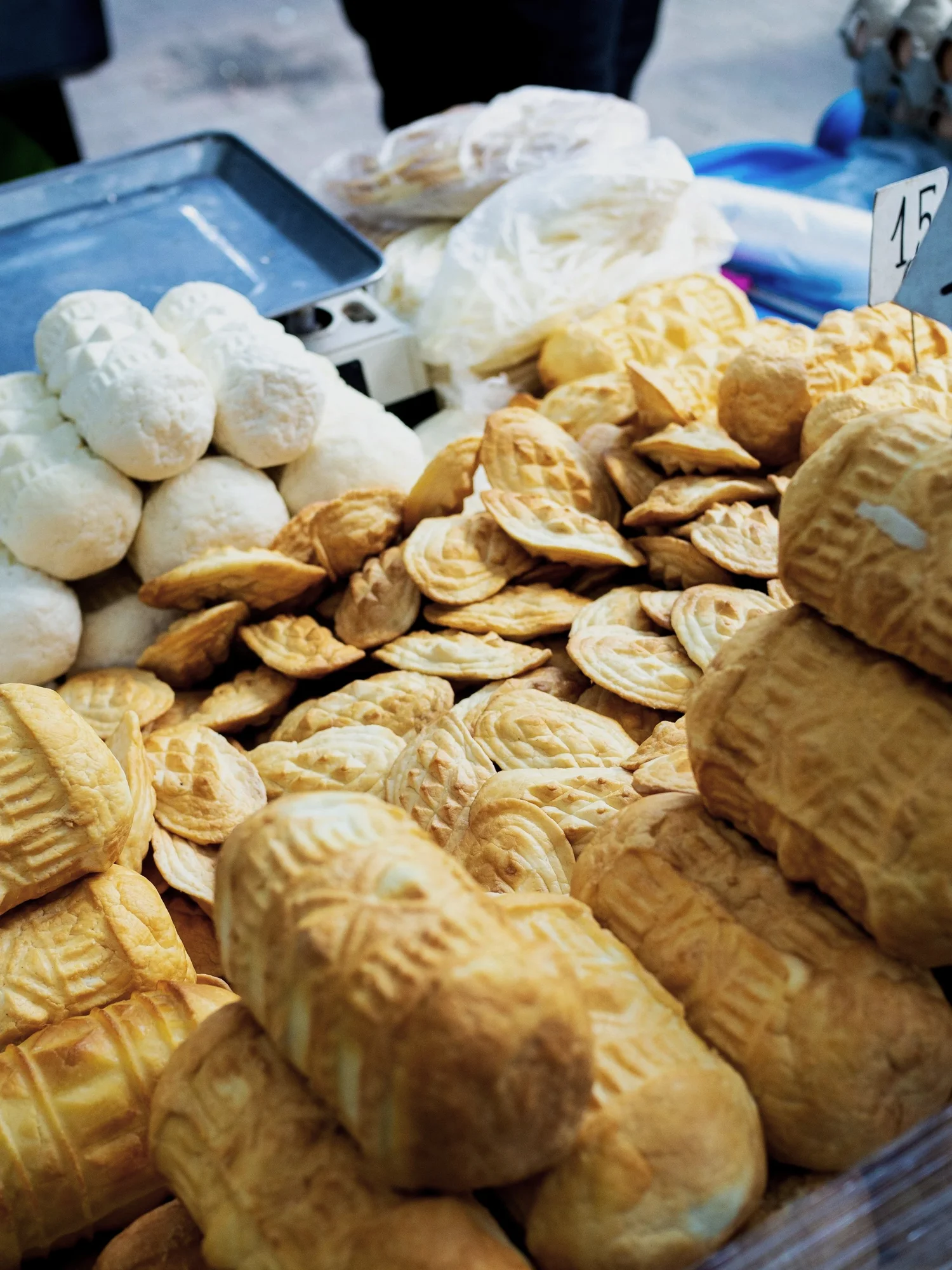 Assorted baked goods including cream-filled pastries, cookies, and bread rolls on a market stall display.