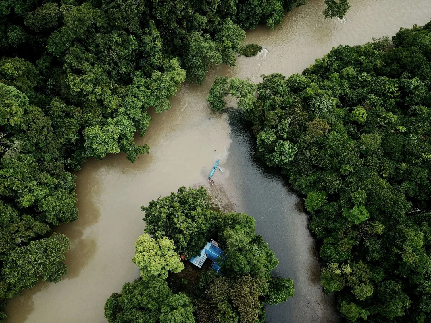 Aerial view of a winding river flowing through dense green forest with a small boat docked at the riverbank.