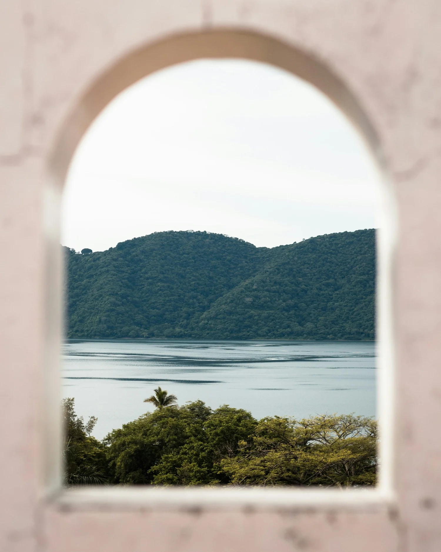 View of a lake surrounded by lush green hills, seen through a small arched window.