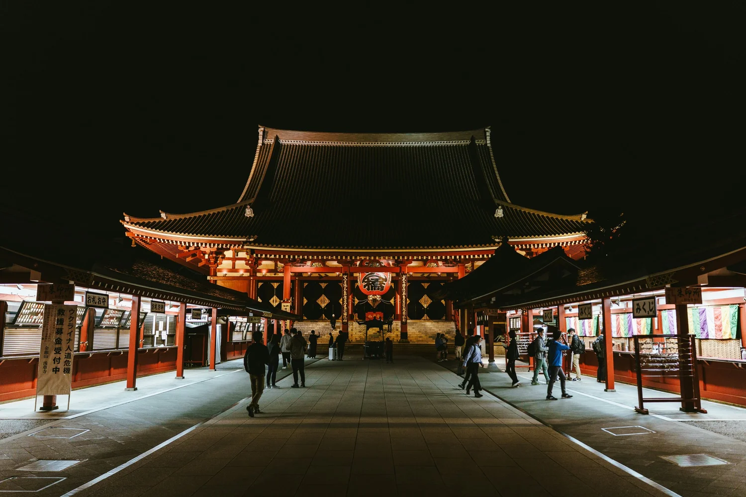 A traditional Japanese temple at night, illuminated with lights, with people walking in the courtyard.