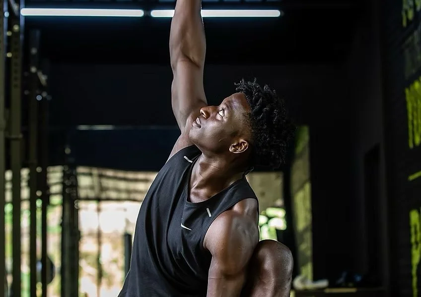 Man doing a yoga pose in a gym, reaching up with one arm.