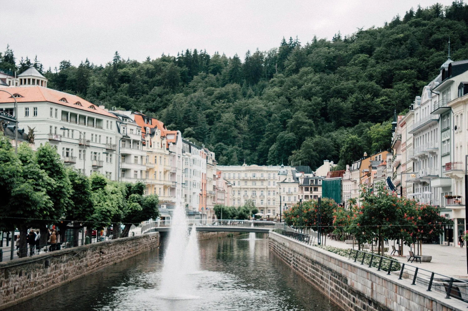 View of a canal in a European city with colorful buildings and a green hillside in the background.