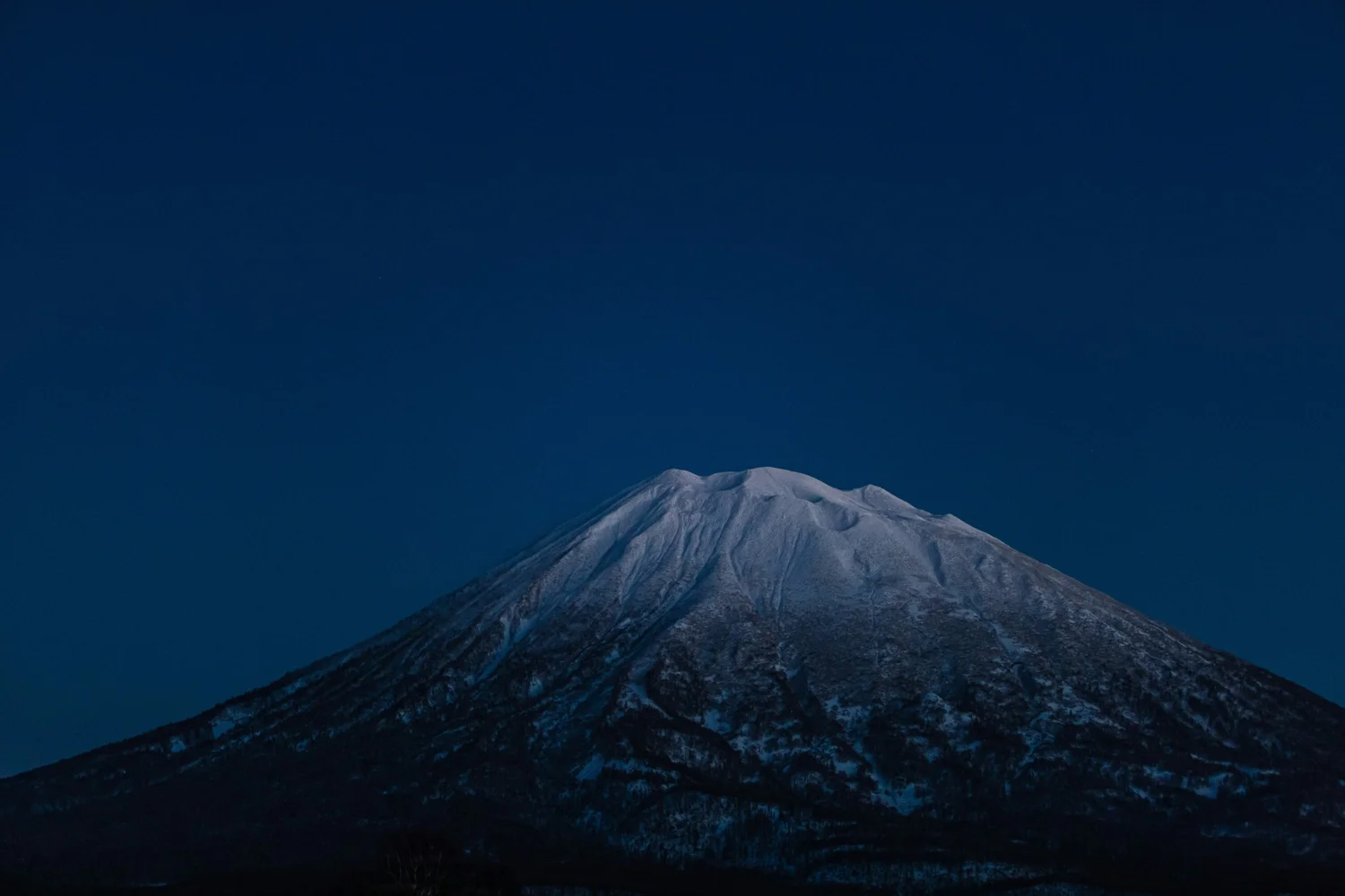 Snow-capped mountain against a clear blue sky at dusk.