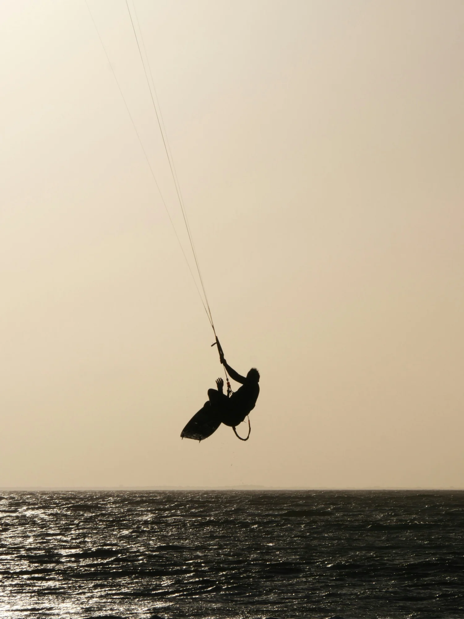 Silhouette of a person kiteboarding over the ocean during sunset