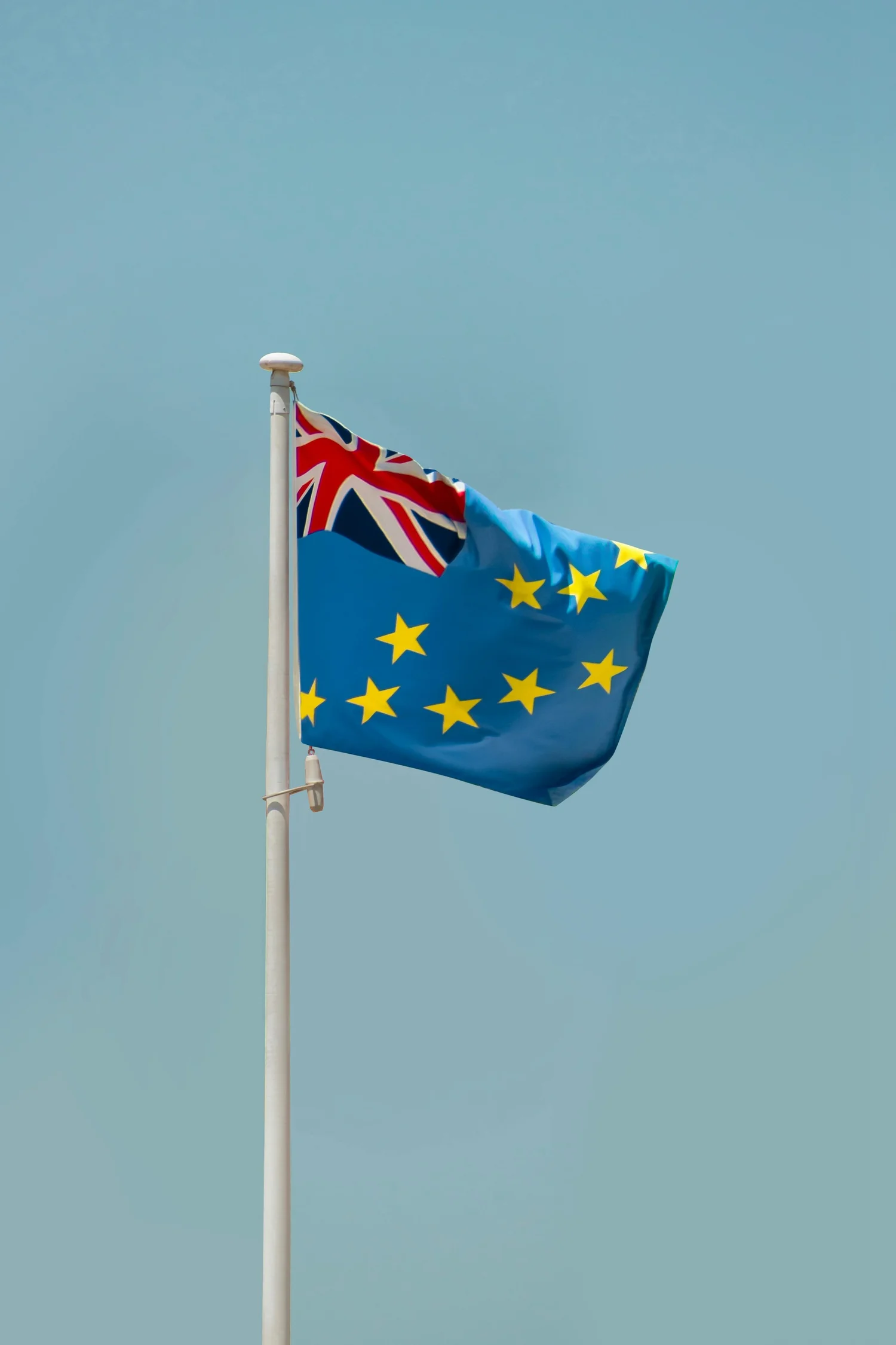 A flagpole flying the Union Jack combined with the European Union flag against a clear blue sky.