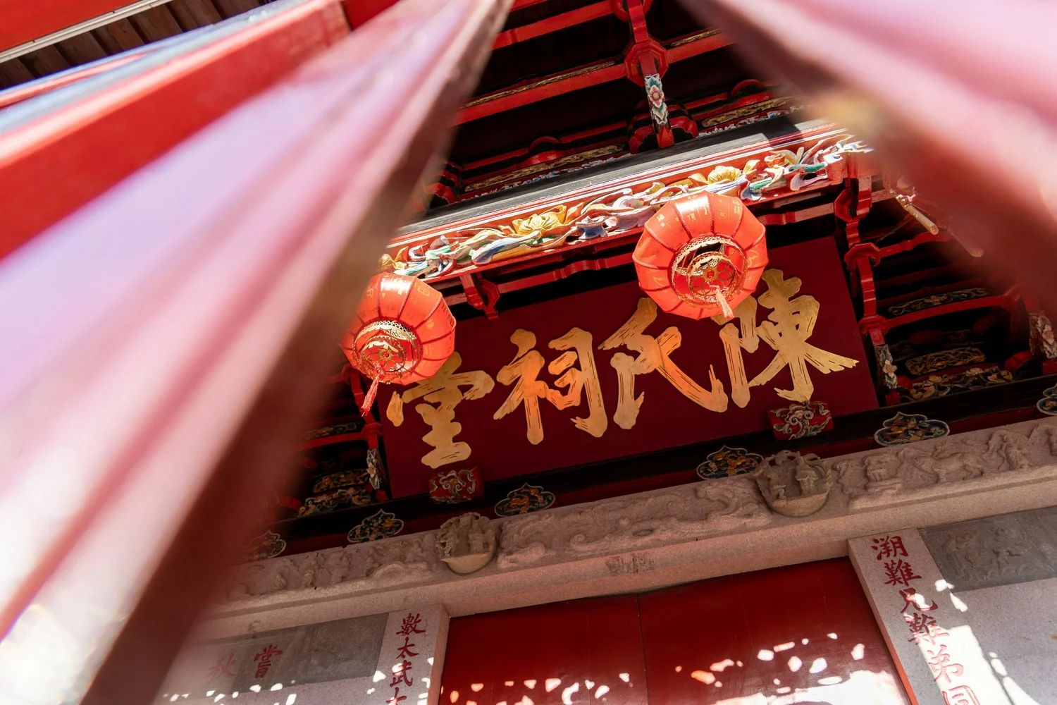 Close-up of a traditional Chinese temple entrance with red lanterns, ornate decorations, and gold Chinese characters on a red signboard.